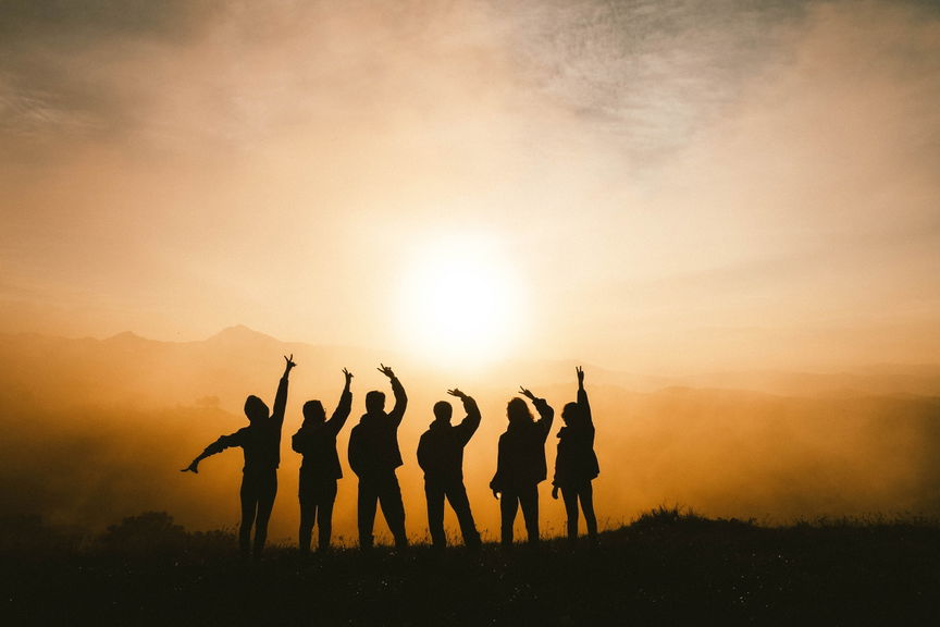 Silhouettes of a group cheering with raised arms on a mountain top at sunset