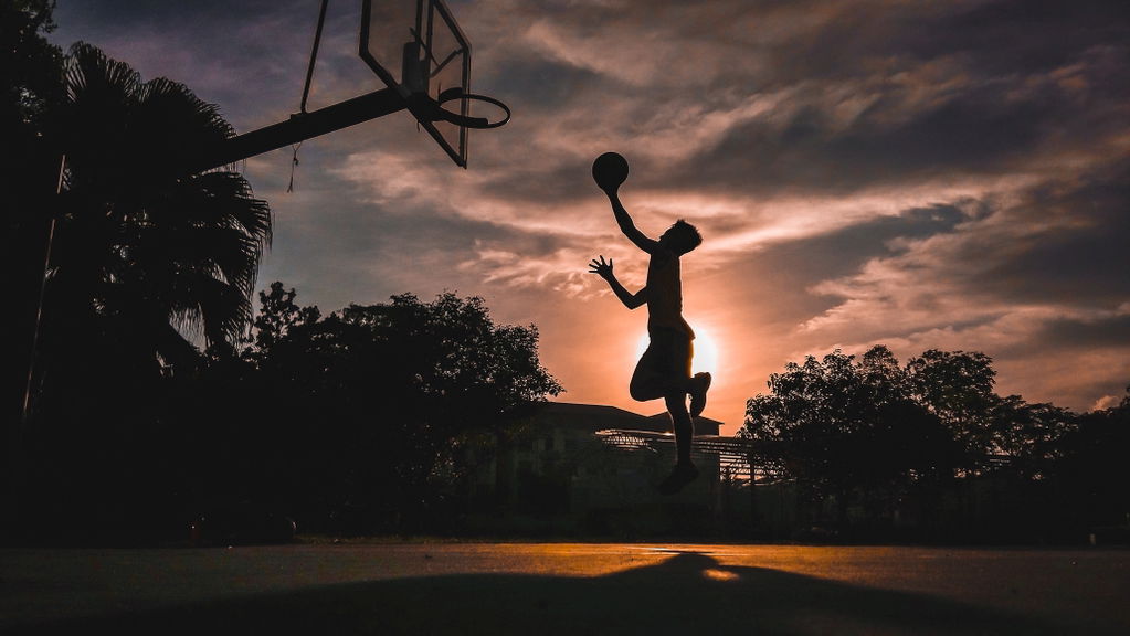 Silhouette of a person leaping to dunk a basketball at sunset