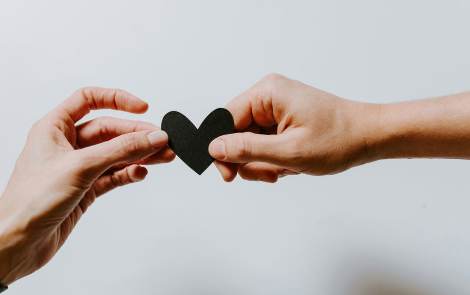 Two hands holding a paper heart between them, symbolising care and connection