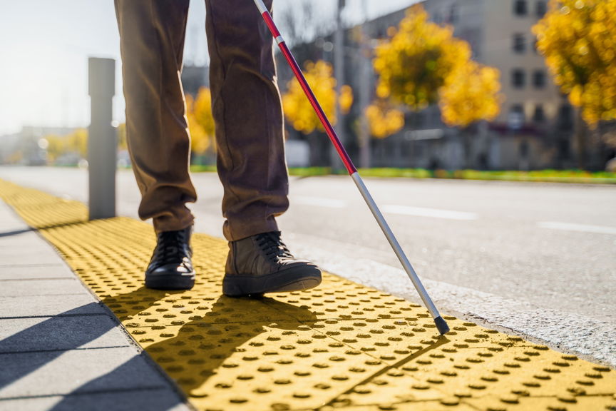 Close-up of a person who is blind using a white cane to walk along a tactile paving path