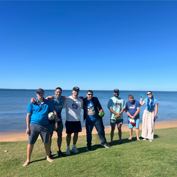 Group of Care to Change team members in blue shirts posing together on the grass by the beach