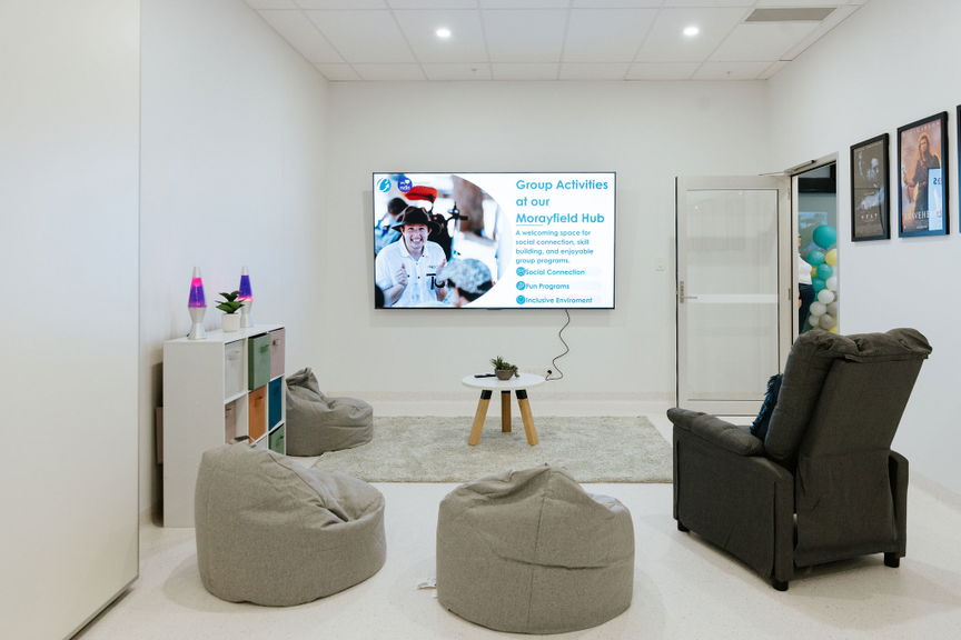 Sensory and gaming lounge with a wall-mounted screen, recliner and bean bags at the Morayfield Hub