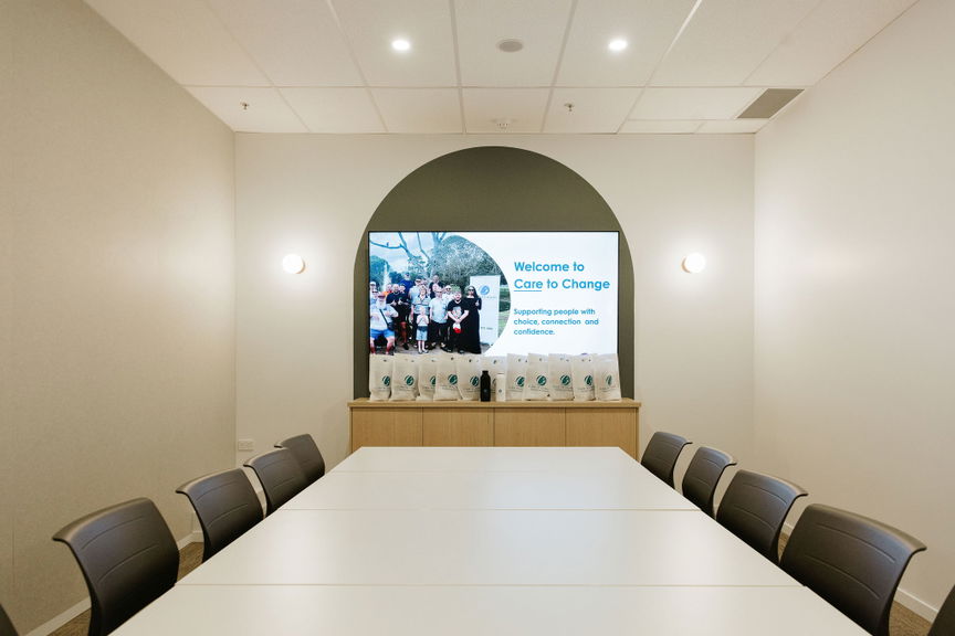 Boardroom with a long meeting table, seating and a wall-mounted presentation screen at the Morayfield Hub