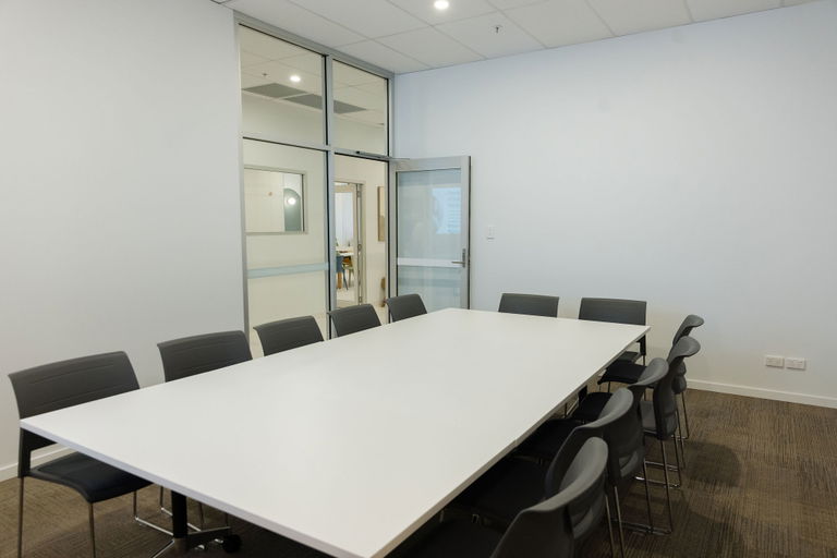Meeting room with a glass wall and white boardroom table at the Morayfield Hub
