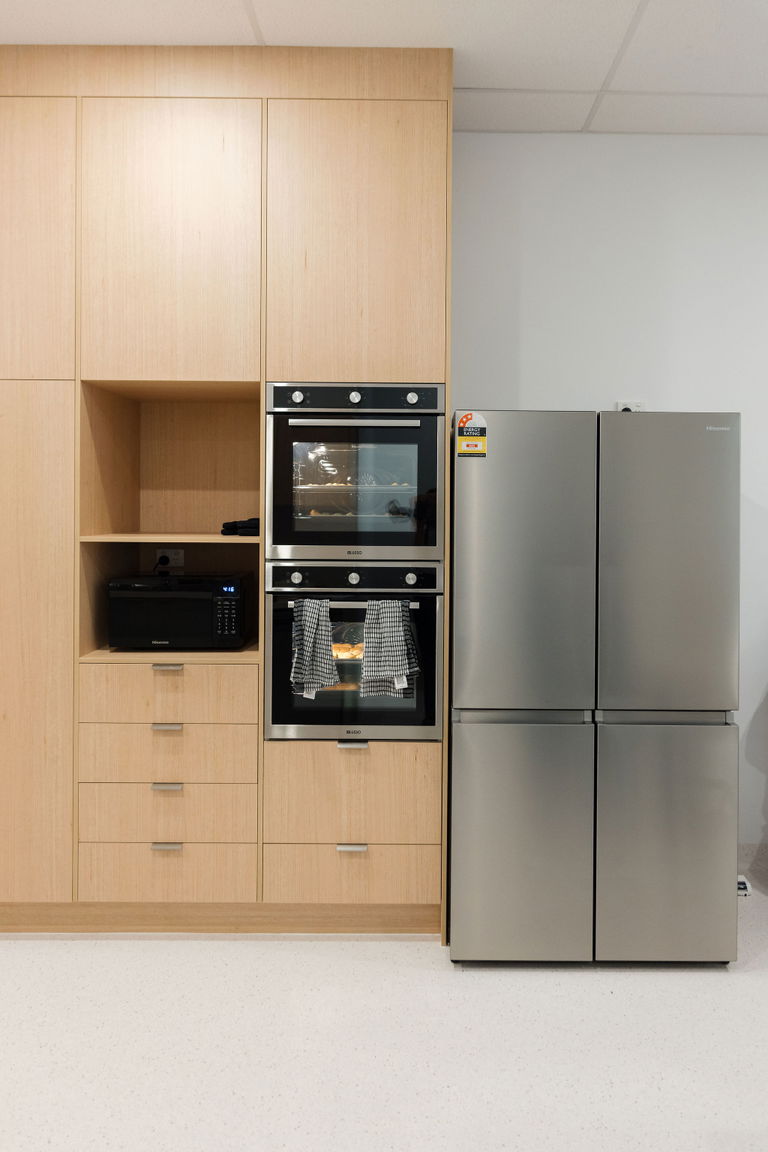 Kitchen cabinetry with a built-in wall oven, microwave and two stainless steel fridges at the Care to Change Morayfield Hub