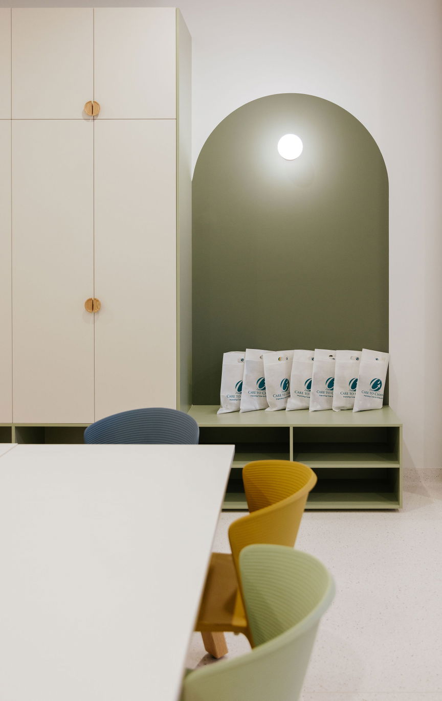 Welcome nook at the Care to Change Morayfield Hub with a sage green arched alcove and branded Care to Change welcome bags lined up on a bench seat beside built-in cabinetry