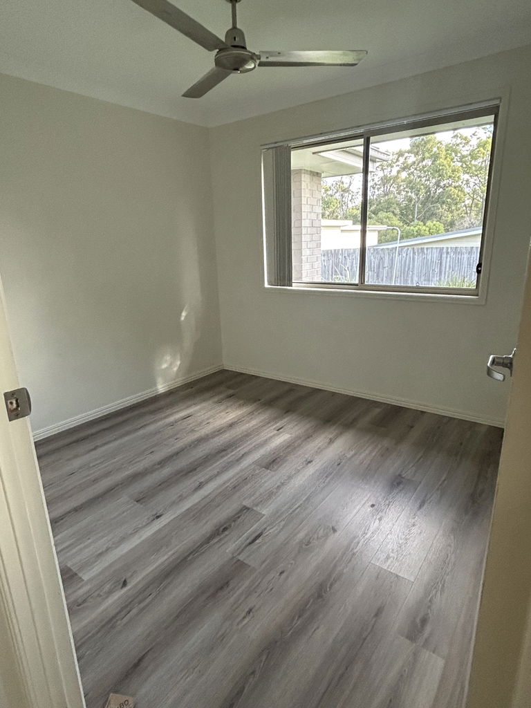 Vacant bedroom with a ceiling fan, window and vinyl plank flooring in the Care to Change supported home in Pimpama